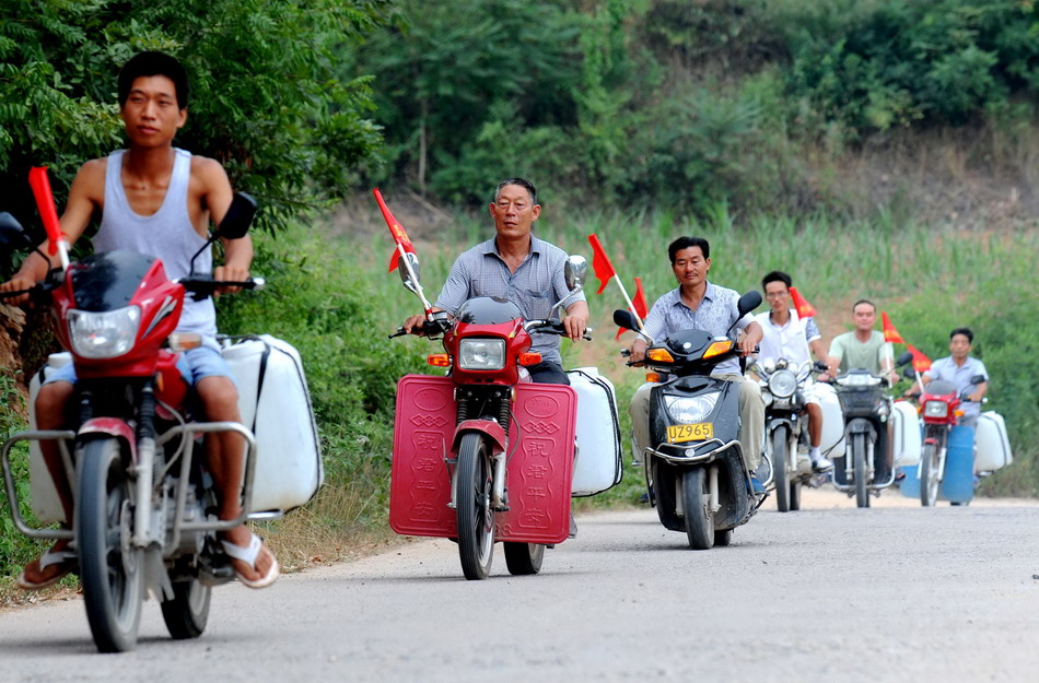 8月5日，河南鲁山县下汤镇爱心送水队队员骑着摩托车送水。