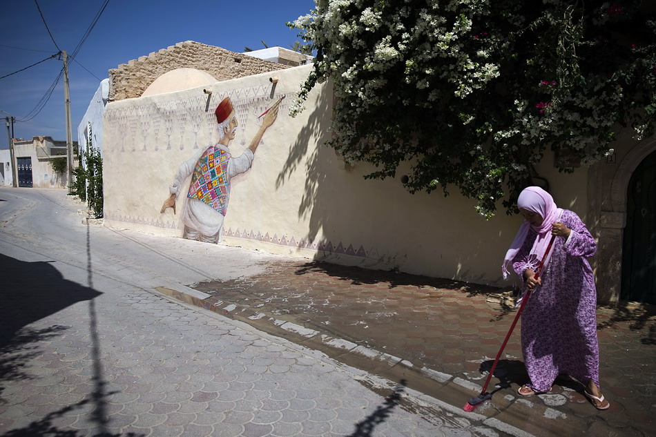  8月7日，在突尼斯杰尔巴岛，一名女子在葡萄牙艺术家马里奥・贝伦创作的壁画旁清扫街道。