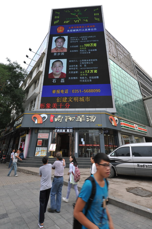 8月17日，在太原市五一广场，行人从曝光“老赖”信息的电子显示屏下走过。