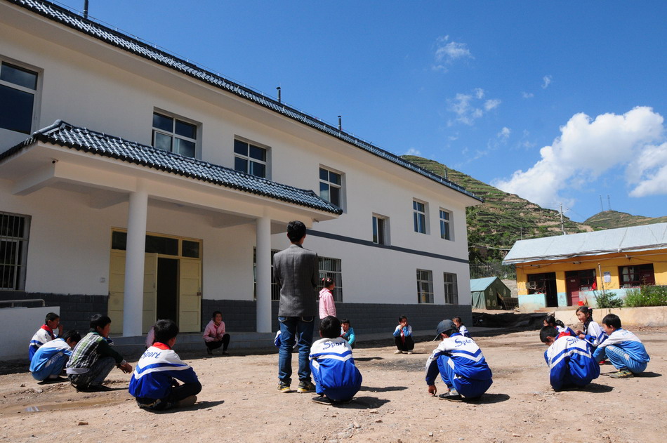 8月28日,一位老师在岷县禾驮乡卓洛小学的新教学楼前给学生上体育课.