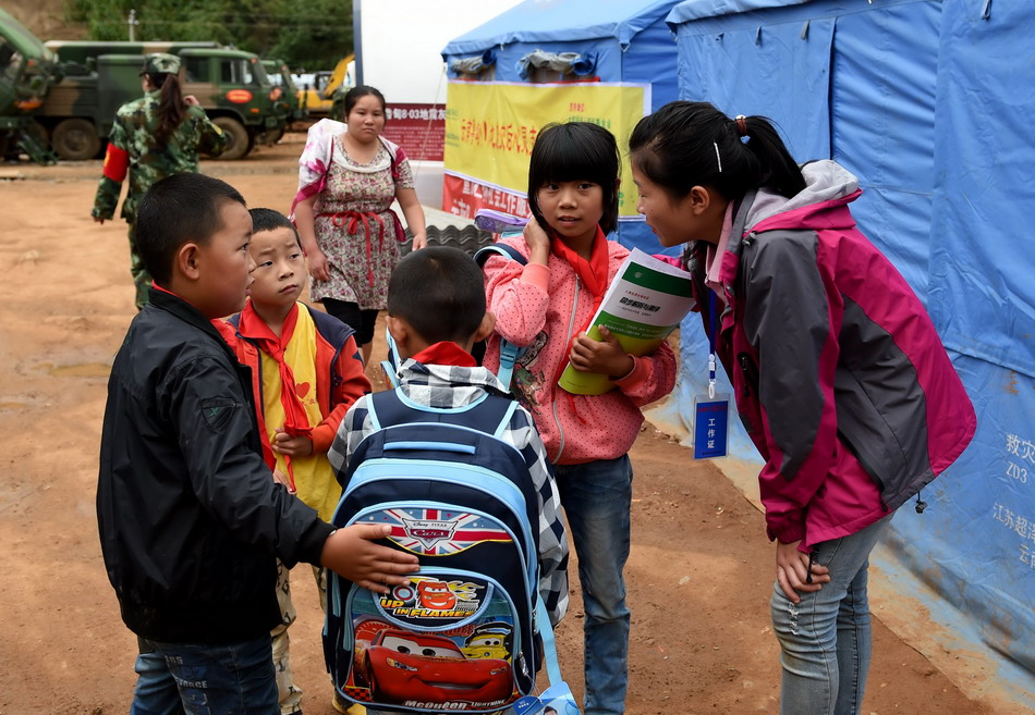  9月2日，一名爱心志愿者（右）在云南鲁甸龙头山镇的灰街子集中安置点与几名小学生聊天。