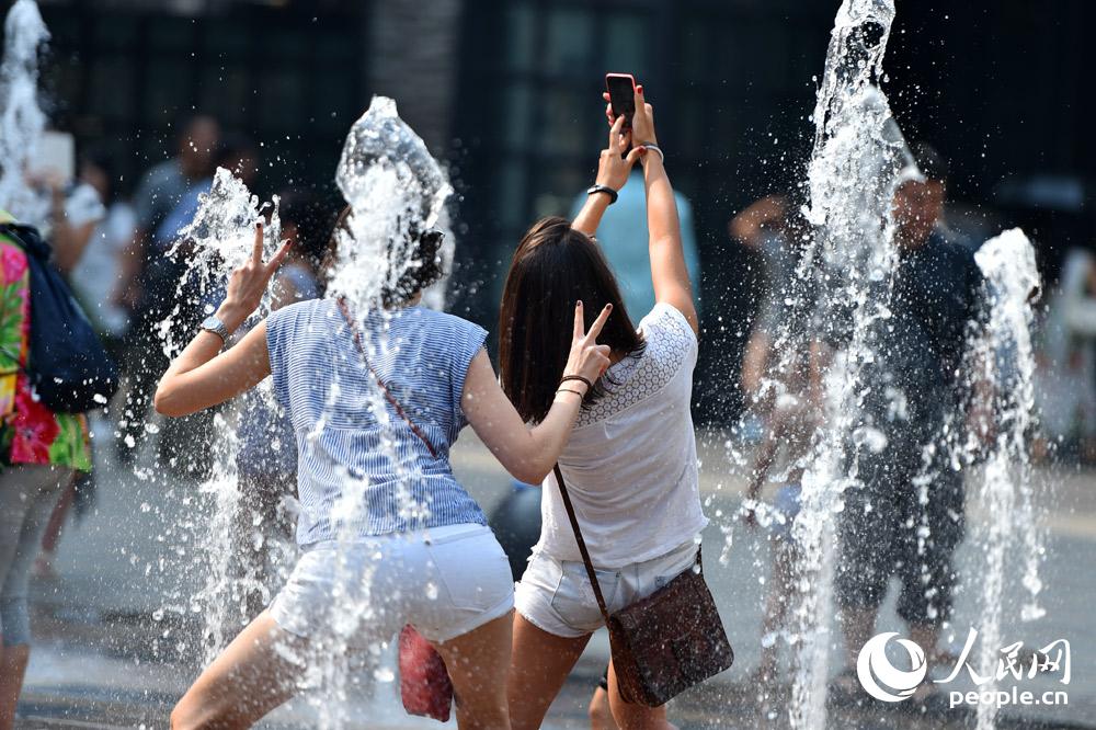 7月12日，北京三里屯，游人为消暑，在喷水池中拍照留影。（人民网记者 翁奇羽 摄）