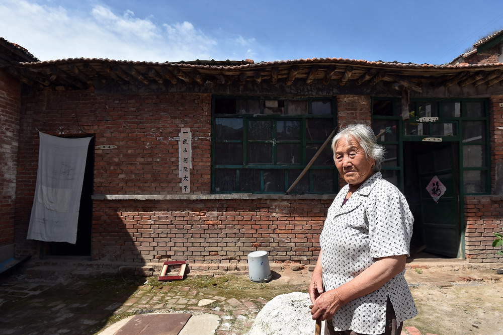 在山西省古交市南社村，村民李丹站在院子里。受煤矿开采影响，她身后的房子向下倾斜，出现多处裂缝，屋顶呈现波浪形状（7月3日摄）。