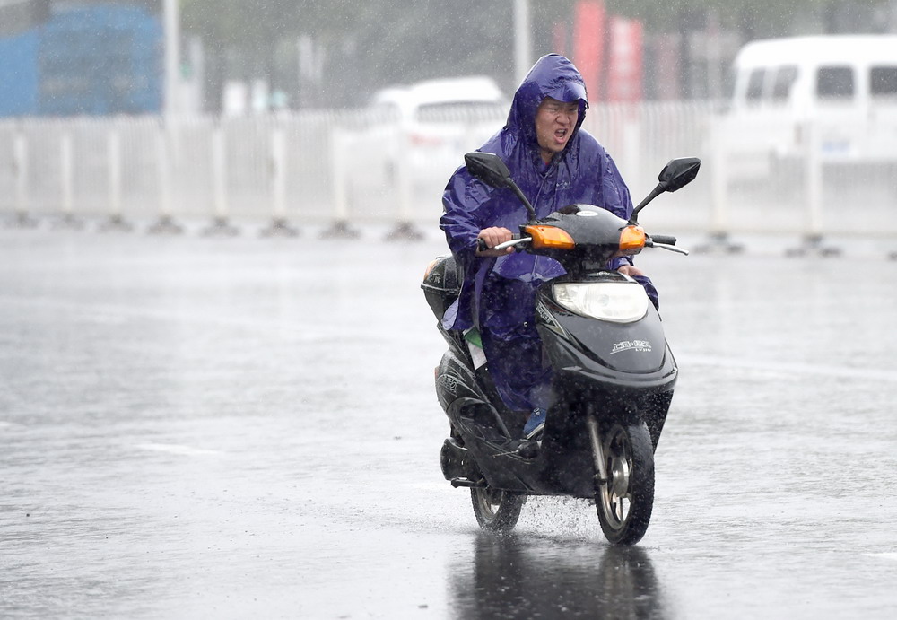 8月10日，合肥市街头，一位路人在雨中骑行。