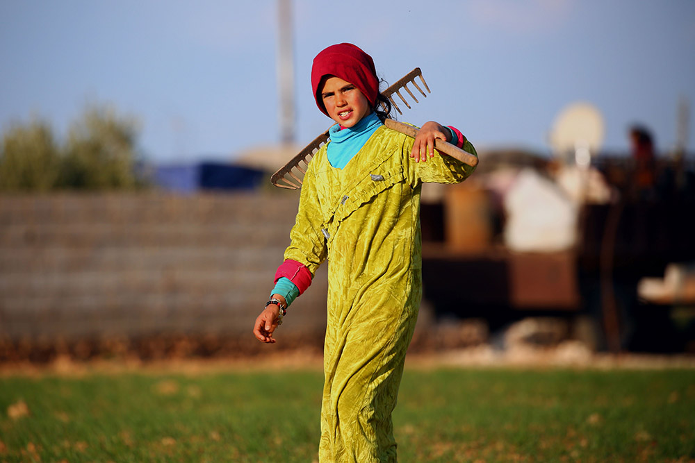 3月7日,在叙利亚城市曼比季南郊的一处临时难民营,一个女孩扛着耙.