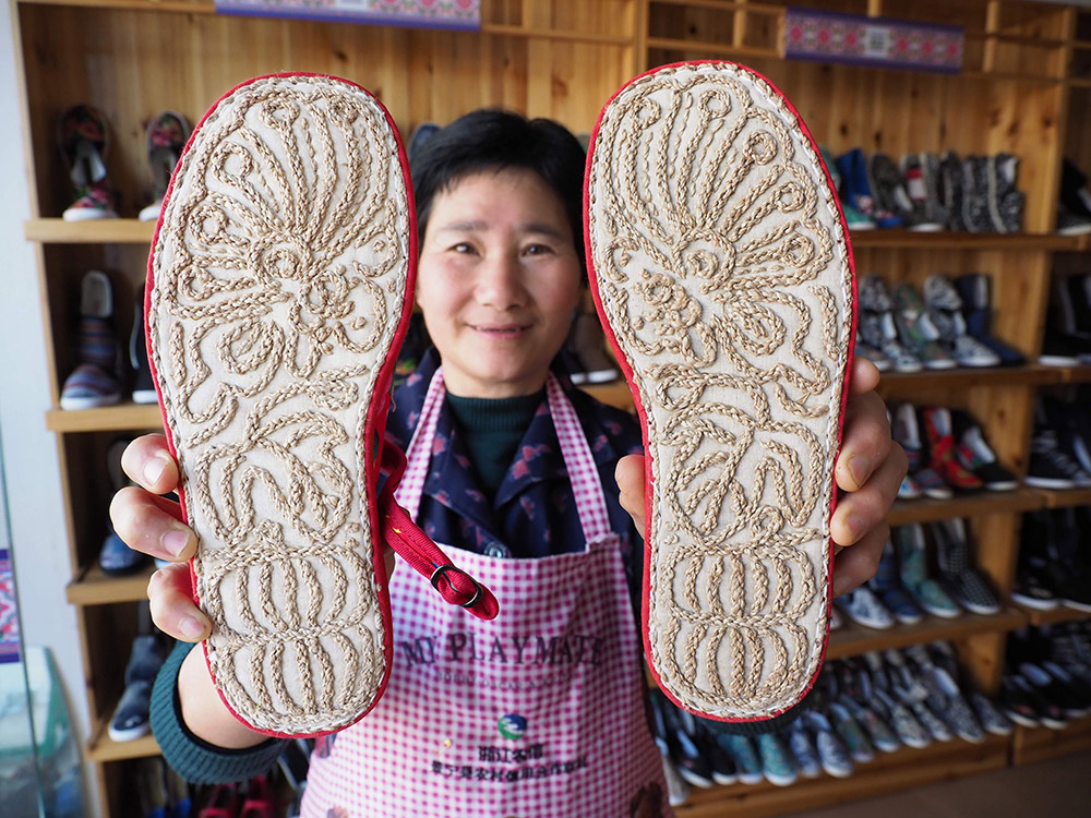 3月15日,在浙江省景宁县一畲族手工布鞋商店,店员王根丹展示一双鞋底