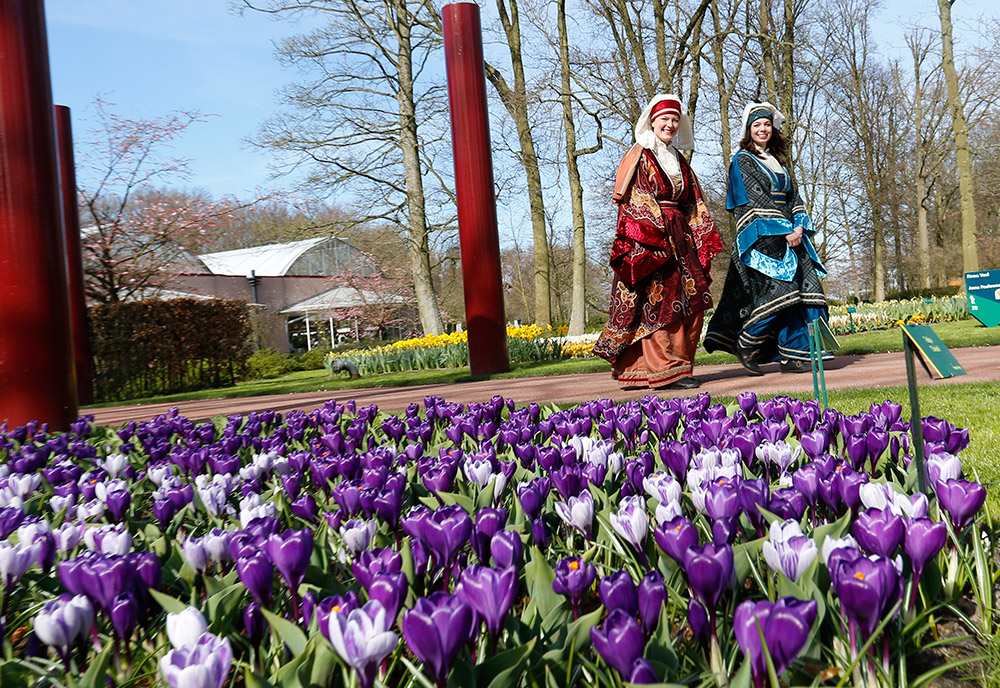 3月21日，在荷蘭利瑟的庫肯霍夫公園入口，身著傳統服裝的人們從郁金香花叢旁走過。