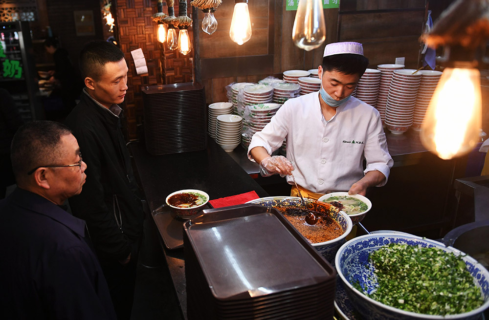 4月12日，在蘭州市城關區阿拉蘭牛肉面主題餐廳，拉面師傅為顧客端上剛剛出鍋的牛肉面。