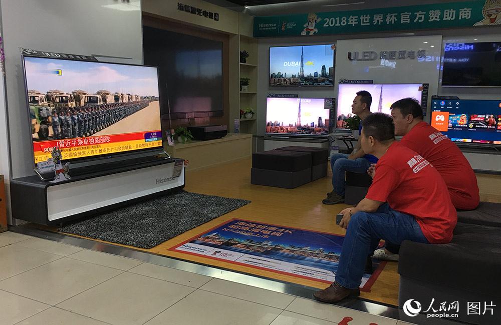 7月30日，在北京某電器城的電視機展櫃，顧客與店員正在觀看慶祝中國人民解放軍建軍90周年閱兵直播。他們表示，為祖國的強盛，感慨自豪！（人民網記者 翁奇羽 攝）