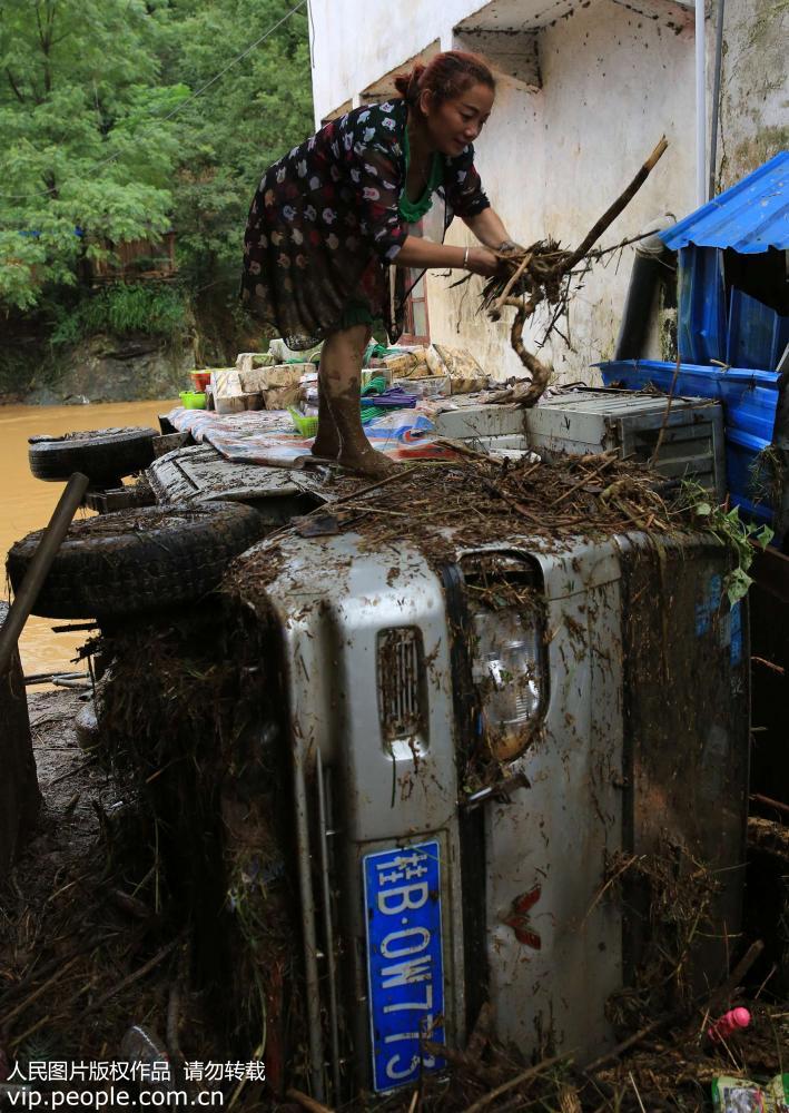 8月12日，在廣西柳州市融水苗族自治縣杆洞鄉杆洞街，村民吳春菊在被洪水淹泡后的汽車上清理洪水雜物。