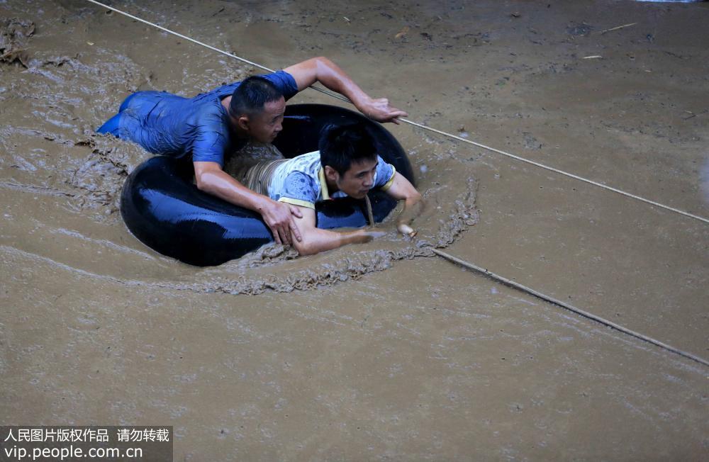 8月13日，在廣西柳州市融水苗族自治縣杆洞鄉杆洞街，救援隊員吳玉雄（藍衣者）正在山洪中轉移一名游人。