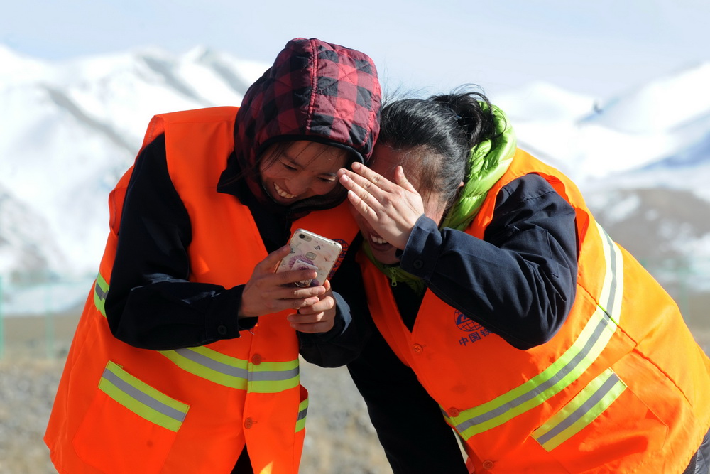 10月23日，信號工李芳（左一）與“大姐”鄭艷工作間隙在昆侖雪山下看手機裡的照片。