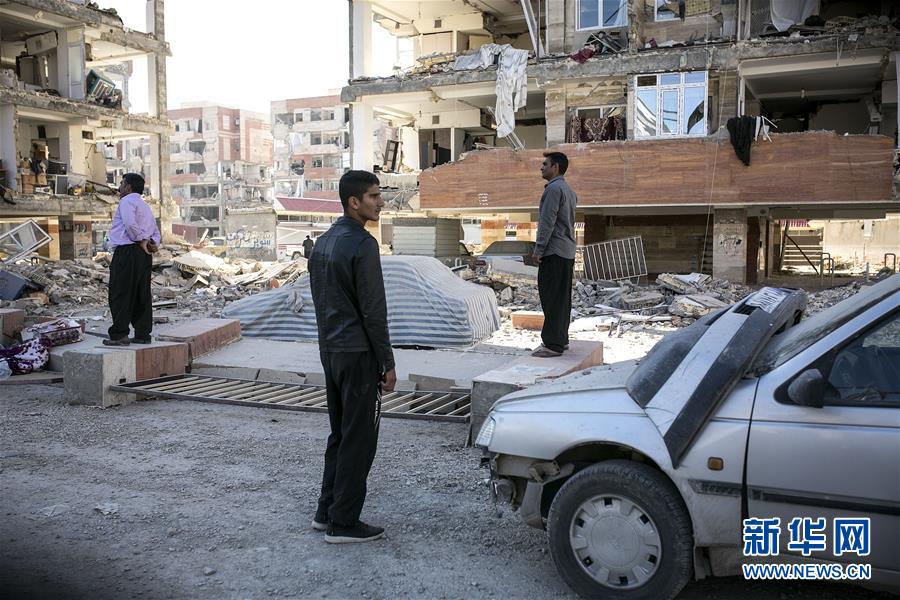 11月13日，在伊朗薩爾波勒扎哈卜，人們站在受損建筑前。