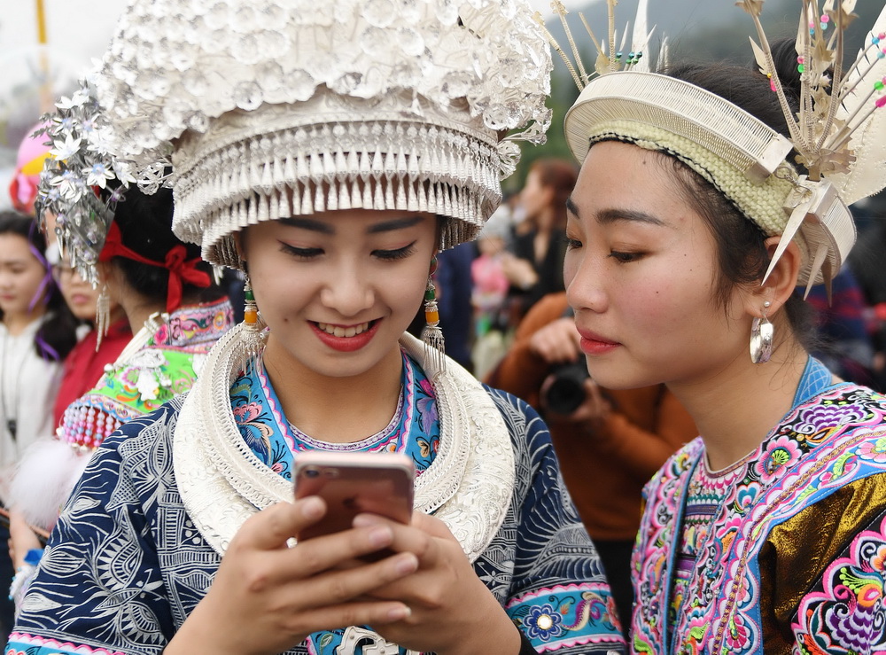 3月3日，在融水苗族自治县香粉乡十六坡会上，苗族姑娘用手机给朋友发送坡会美景。