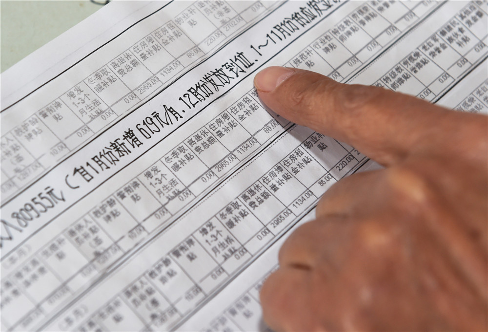 青岛退休教师张伟源在家中介绍工资条构成明细（3月8日摄）。