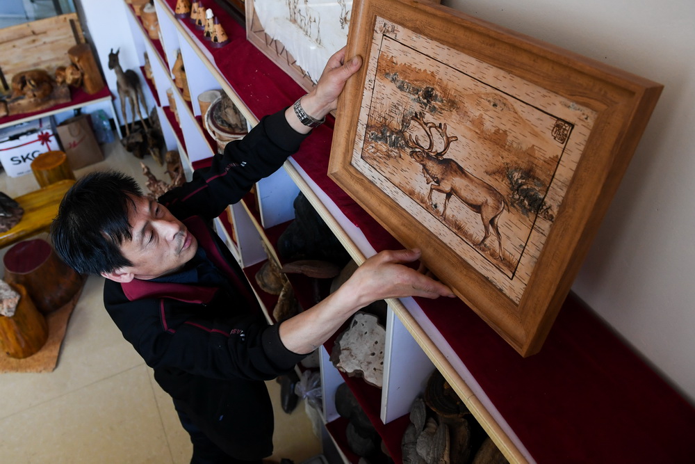 6月7日，在内蒙古自治区根河市的工作室里，王跃辉摆放一件驯鹿觅食的桦树皮工艺品。