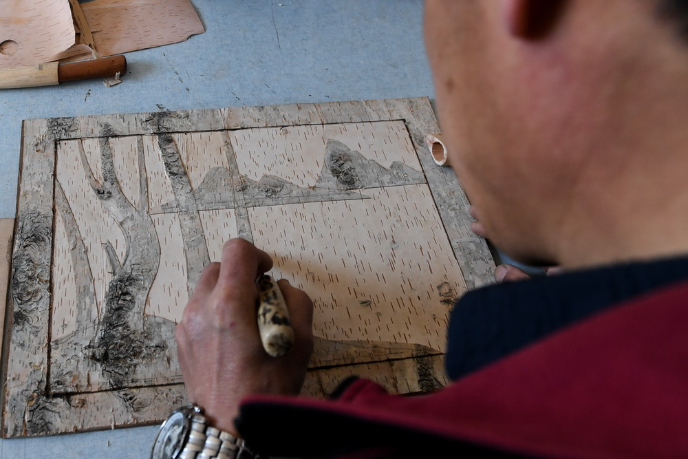 6月7日，在内蒙古自治区根河市的工作室里，王跃辉在桦树皮上雕刻山、树等图案。