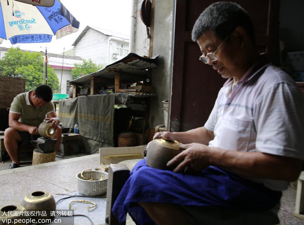 6月19日，在張家界市慈利縣溪口鎮，民間工匠譚福林（右）和他的兒子譚俊杰在制作手工銅壺。