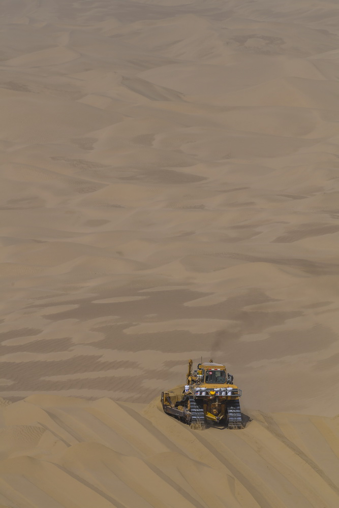 一台大型推土机在地处塔克拉玛干沙漠深处的施工现场平整沙丘（7月10日摄）。