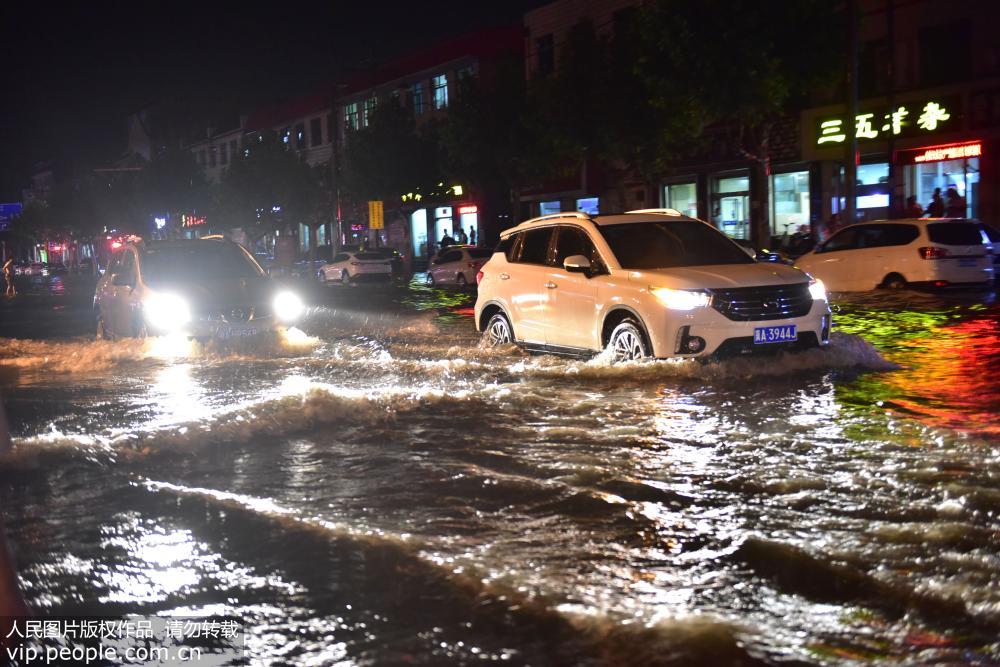 7月18日晚，在河北省石家庄新樂市新華路上，汽車在大水中前行。