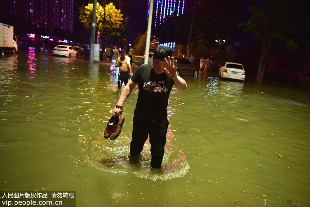 7月18日晚，在河北省石家庄新樂市新華路上，行人在大水中提著鞋子前行。