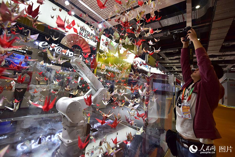 11月5日，在进博会日本三菱展台，媒体记者拍摄正在表演扇子舞的智能机械臂。（人民网记者 翁奇羽 摄）
