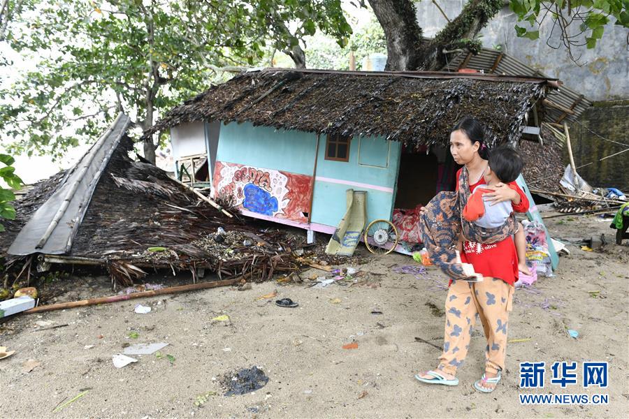12月23日，在印度尼西亞萬丹省卡裡塔，一名女子抱著孩子從一處建筑殘骸旁走過。 印度尼西亞抗災署23日說，印尼西部巽他海峽海嘯死亡人數已經上升到168人。印尼西部巽他海峽22日晚發生海嘯。海嘯發生時當地沒有監測到地震活動，初步懷疑海嘯是由喀拉喀托火山噴發引發海底岩層滑坡和月圓引發漲潮共同所致。 新華社發（韋寧攝）