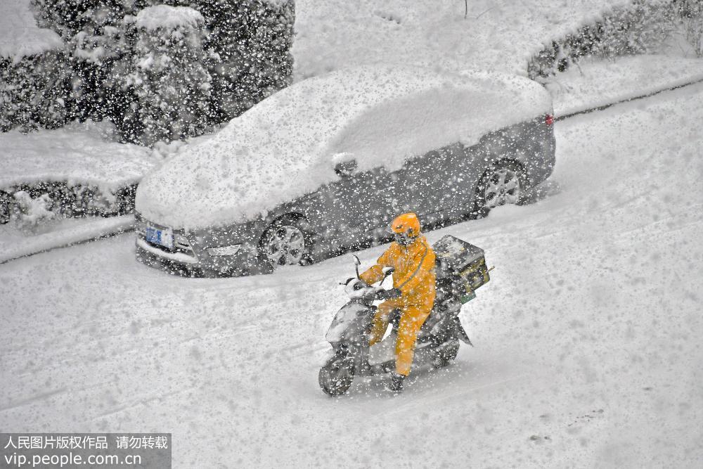 12月27日，行人在山東省煙台市福山區街頭冒雪出行。