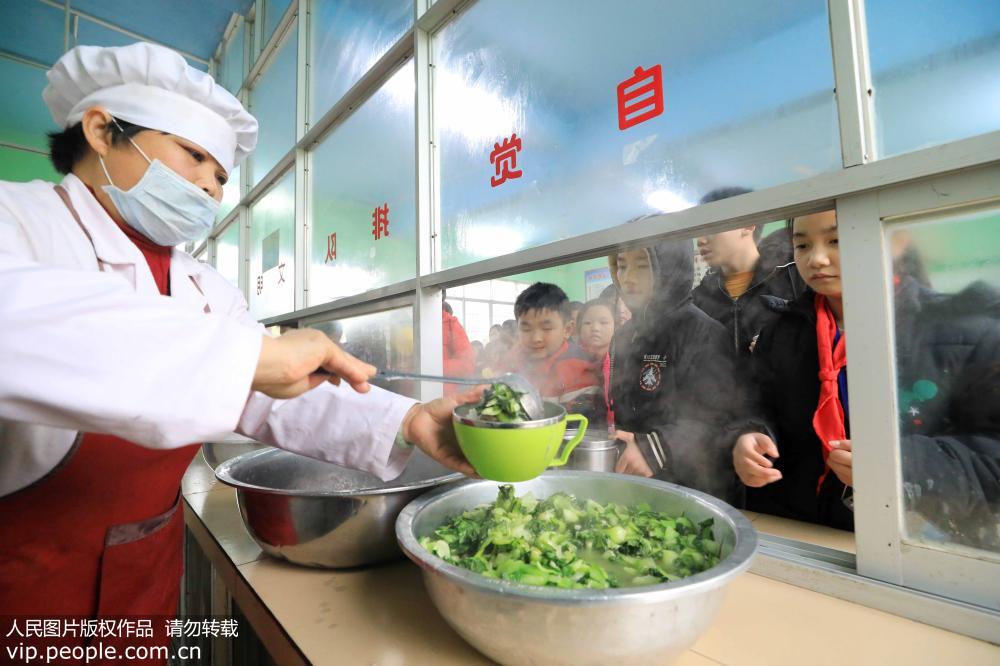 2月18日，在广西柳州市融安县大坡乡岗伟村小学，一名工作人员在为学生分“免费午餐”。
