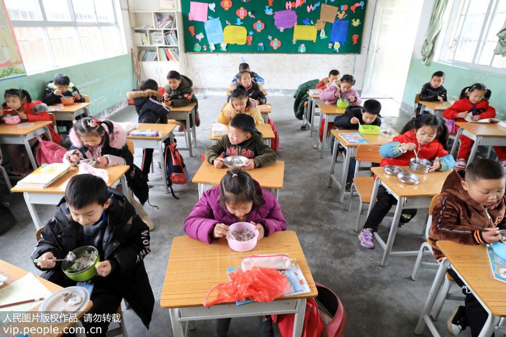 2月18日，在廣西柳州市融安縣大坡鄉崗偉村小學，學生們在教室內吃“免費午餐”。