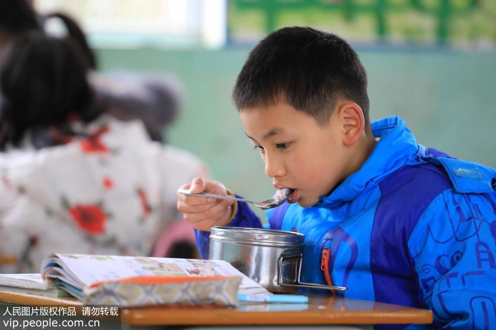 2月18日，在廣西柳州市融安縣大坡鄉崗偉村小學教師，一名學生邊吃“免費午餐”邊看書。