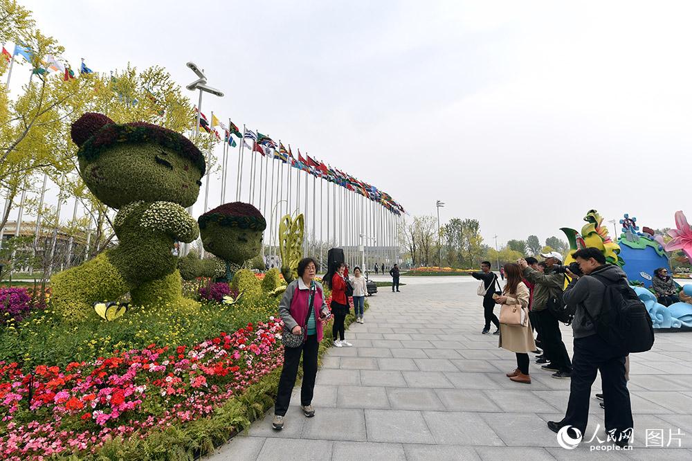 4月29日，游客在世园会吉祥物“小萌芽”和“小萌花”的主题花坛前拍照留念。