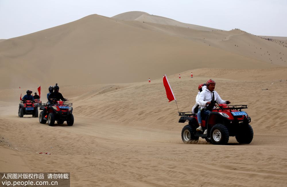 2019年5月2日，游客在甘肅省敦煌市鳴沙山月牙泉景區乘坐沙漠越野摩托車欣賞大漠風光。