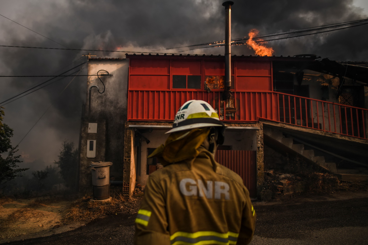 7月21日，在葡萄牙中部的羅達村，一名消防人員站在燃燒的房屋前。