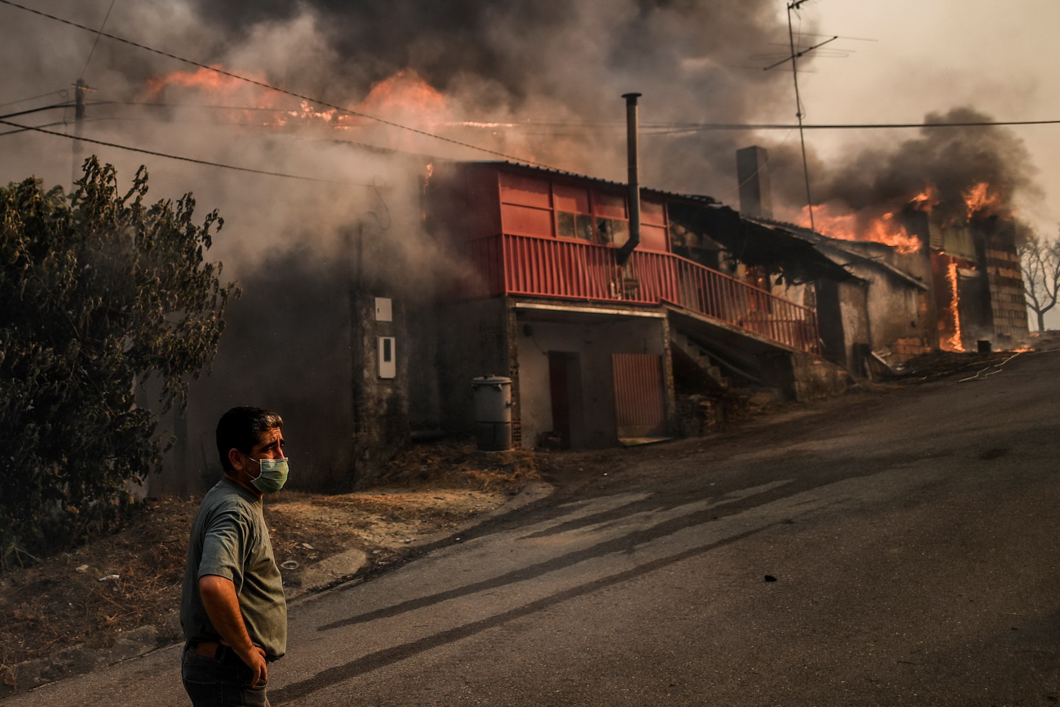 7月21日，在葡萄牙中部的羅達村，一名戴口罩的村民站在燃燒的房屋前。
