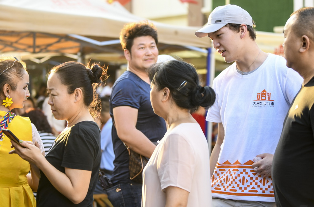 7月24日，志願者葉迪力·夏力哈爾（右二）在大巴扎景區引導游客排隊購物。