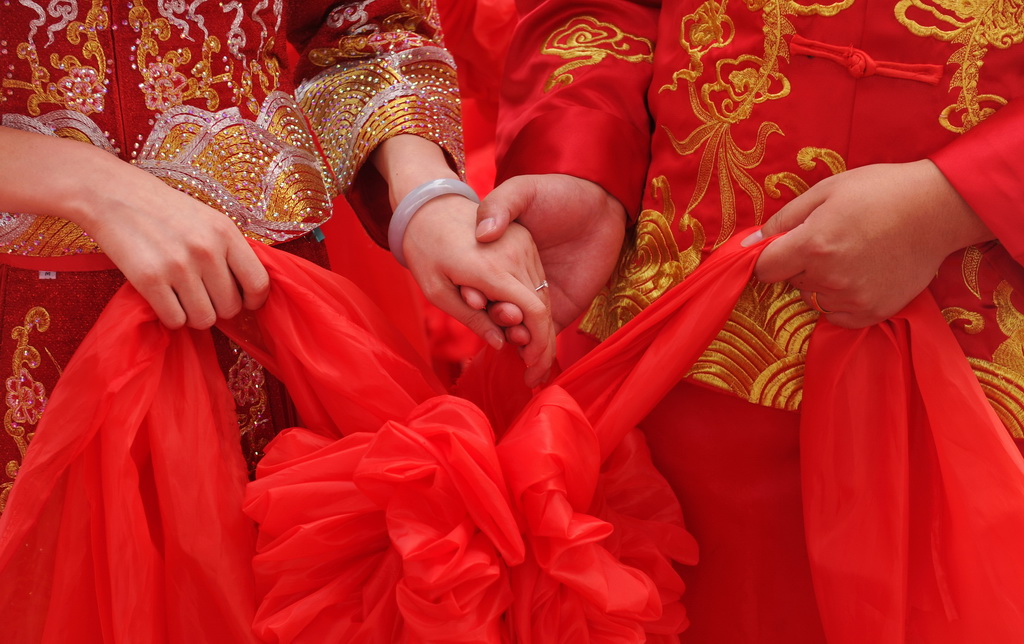 8月6日，在河北黃驊南海公園舉辦的“執手幸福·為愛減負”大型公益集體婚禮上，一對新人手持紅繡球牽手。