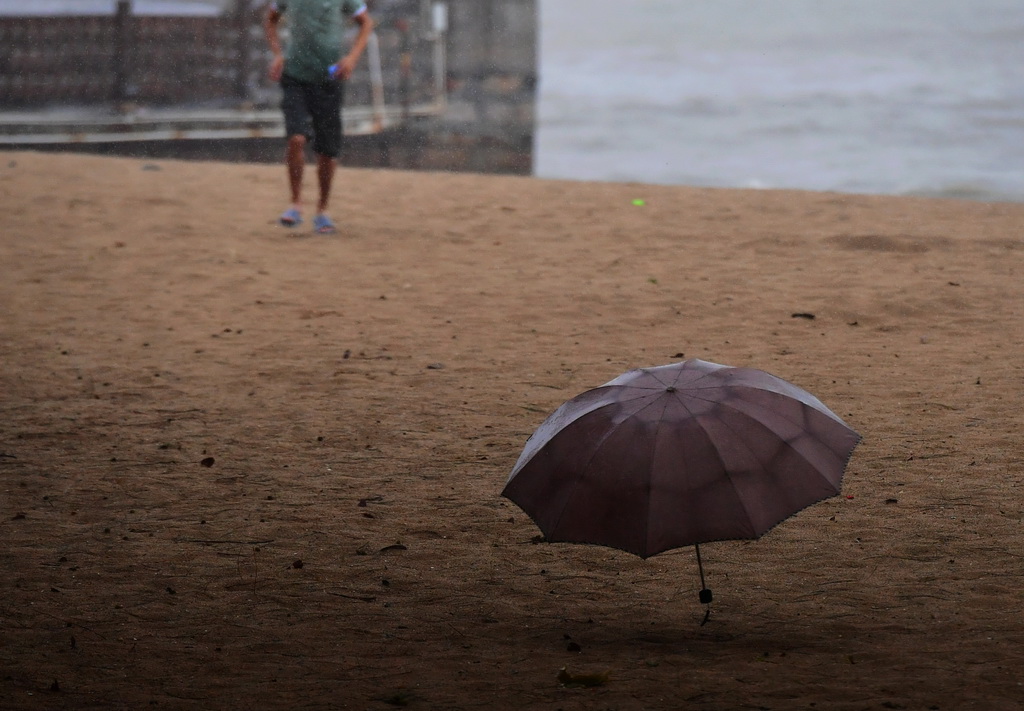 8月25日，在廈門一處海邊沙灘上，市民追著被大風刮跑的雨傘。