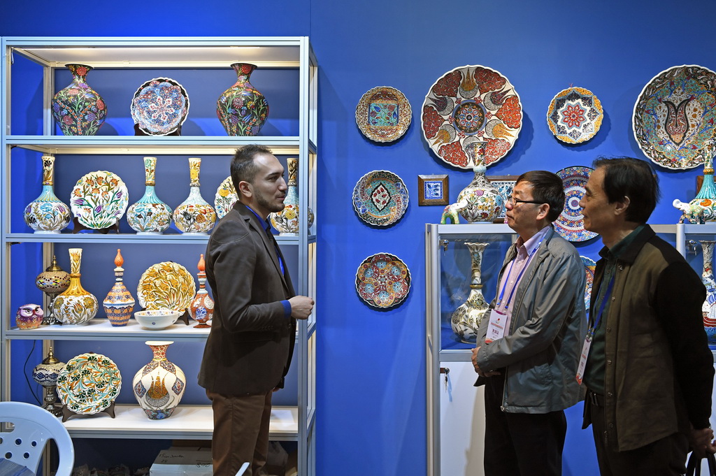 在中國景德鎮國際陶瓷博覽會的現場，來自土耳其的參展商（左一）與參觀者交流（2018年10月18日攝）。新華社記者 萬象 攝