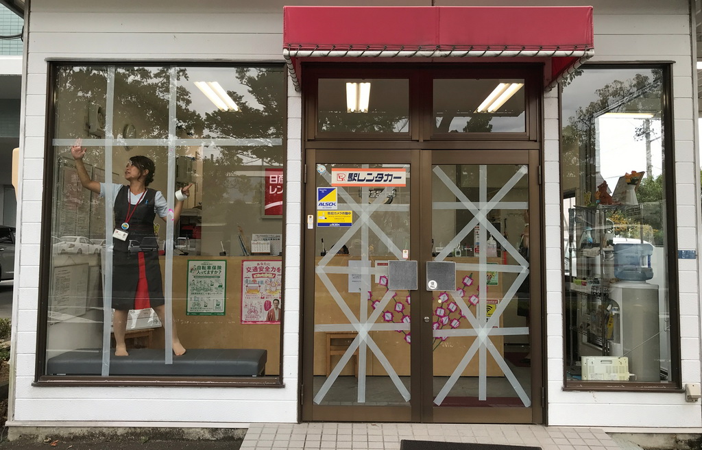 10月11日，在日本静冈县挂川，一名商店店员在玻璃上贴胶带，防止玻璃窗在即将到来的台风中受损。新华社/路透