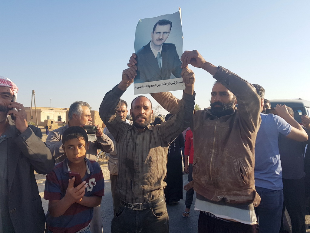 10月14日，在敘利亞北部哈塞克省，當地民眾手持敘利亞總統巴沙爾·阿薩德畫像，慶祝敘政府與庫爾德武裝達成協議。