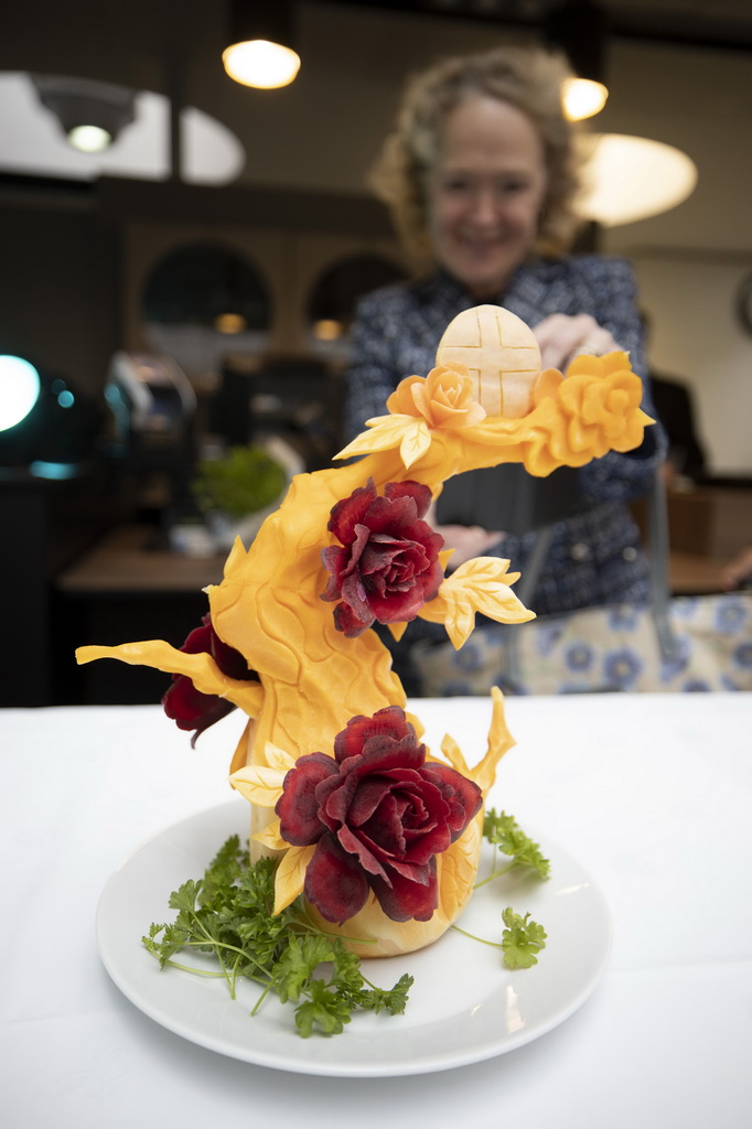 10月14日，在芬兰赫尔辛基的邮政大楼餐厅内，芬兰农业林业部常务秘书胡苏-卡利奥观看中国烹饪协会厨师雕刻的菜品《花前月下》。