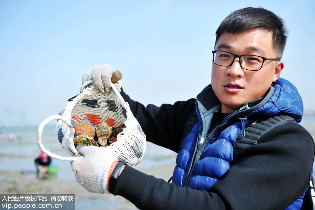 10月30日，山東青島西海岸新區唐島灣南岸海灘，一位游客在展示自己趕海的收獲。