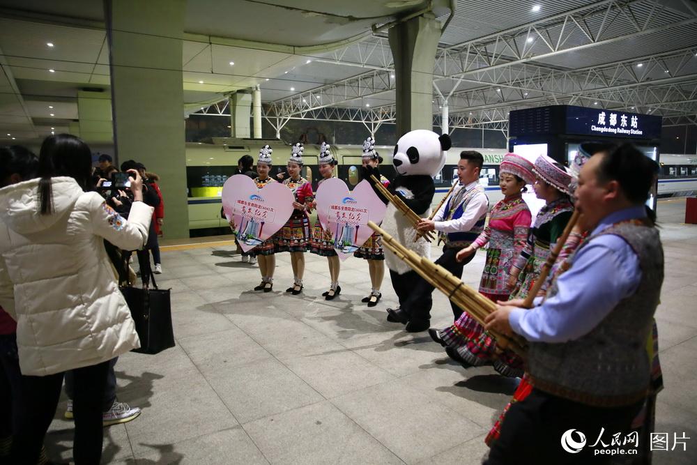12月16日，旅客們舉起手機記錄身著苗族服飾和“熊貓服”的工作人員。（李鍇 攝）