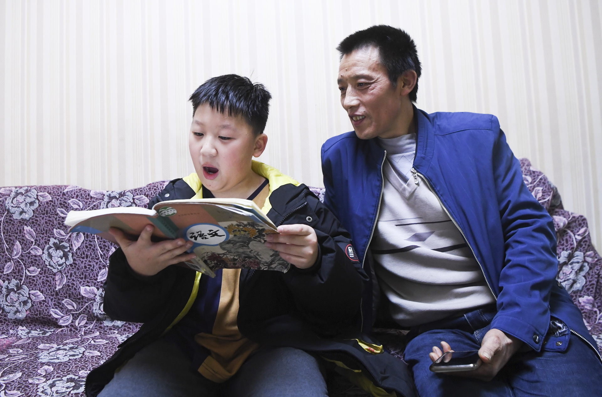  晚飯后，12歲的兒子冉俊超在家裡朗誦課文，冉光輝在一旁聽（1月5日攝）。