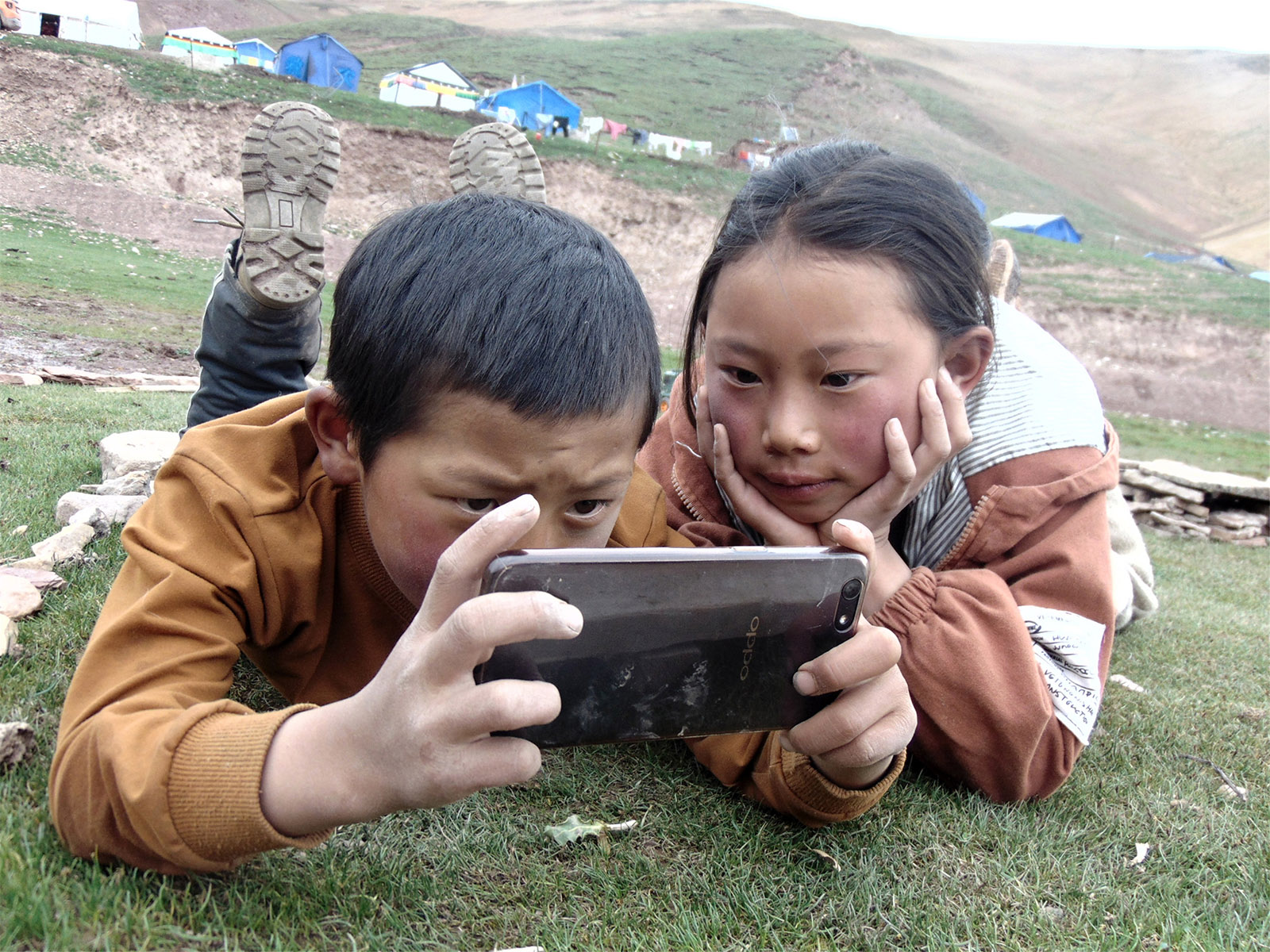 措拉毛(高中組)青海《美好一刻》 鄰居家的弟弟妹妹拿著父親的手機，靜靜的趴在草原上，看著自己用手機拍的照片，享受這美好的幸福生活。搜索復制