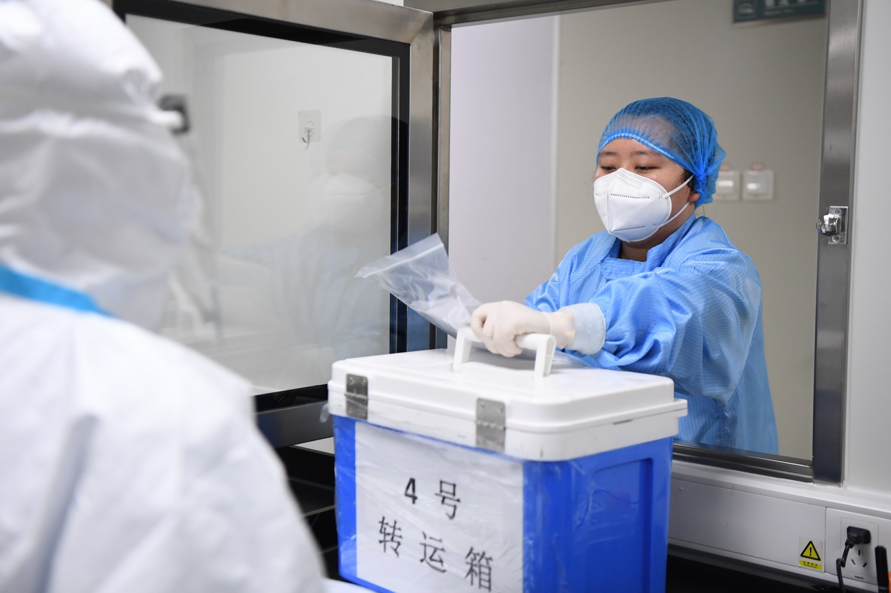 3月10日，长沙卫实医学检测所的工作人员（右）将采集回来的新冠肺炎核酸检测样本传递进入前处理室。