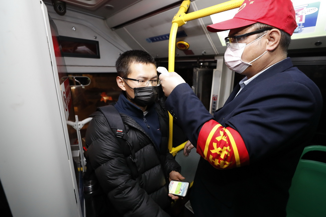 3月25日，在武昌火车站综合体站始发的首趟518路公交车上，安全员给乘客测量体温。