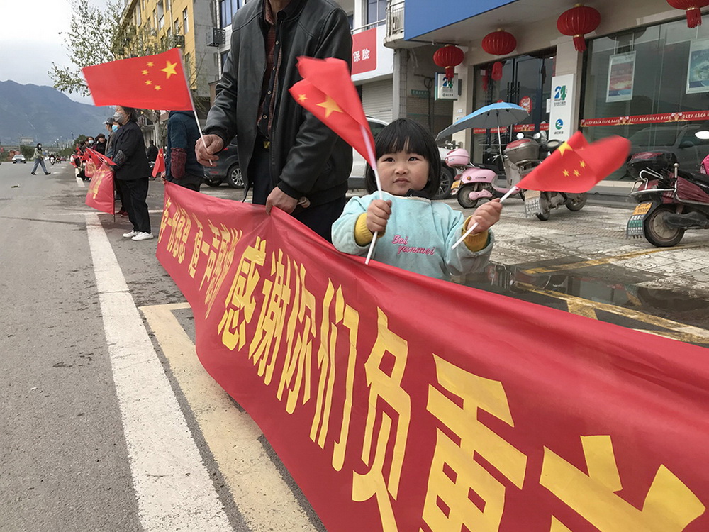 26.3月28日，仙居縣群眾拉起橫幅，揮動紅旗，夾道迎接英雄回家。徐小鳳 攝