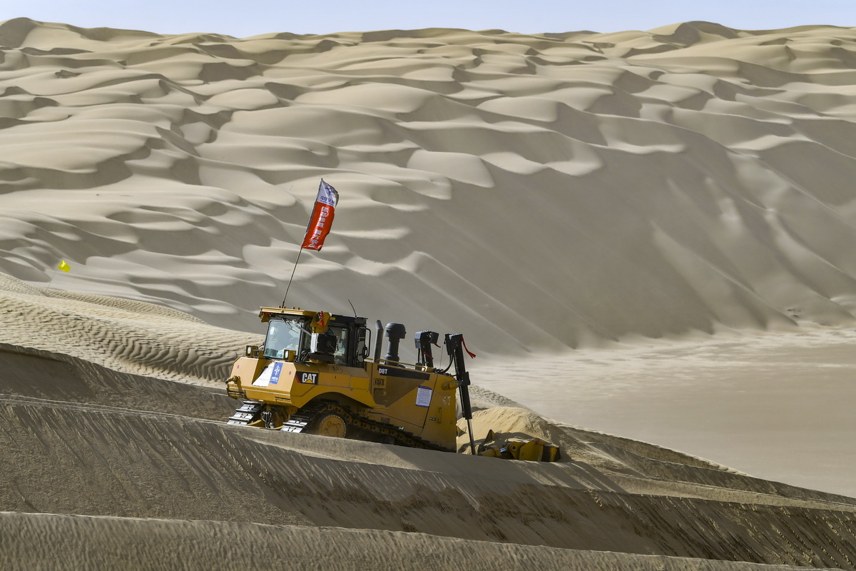 在新疆尉犁至且末沙漠公路施工现场，工人驾驶大型推土机推平沙山（5月16日摄）。
